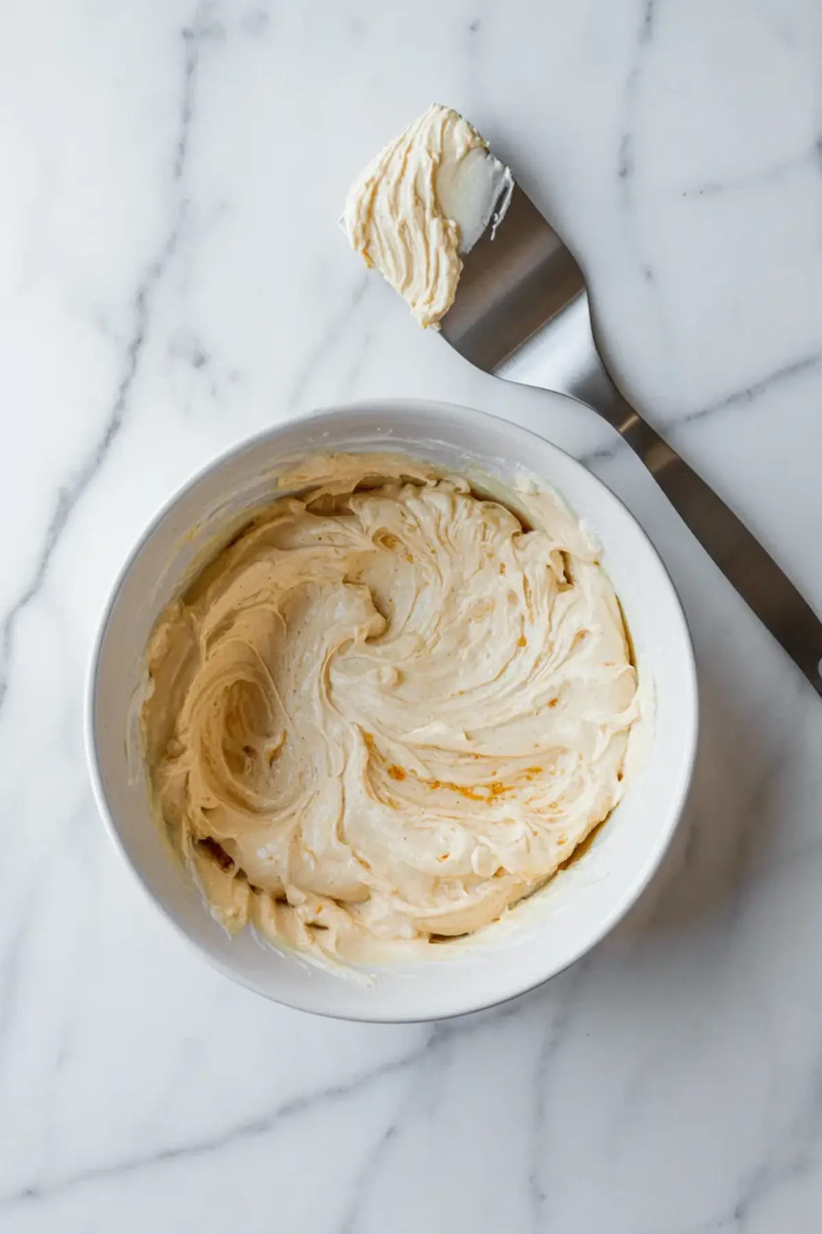 Whipped cream cheese dip mixture in a bowl with a spatula, showing the smooth base before the cranberry topping is added.