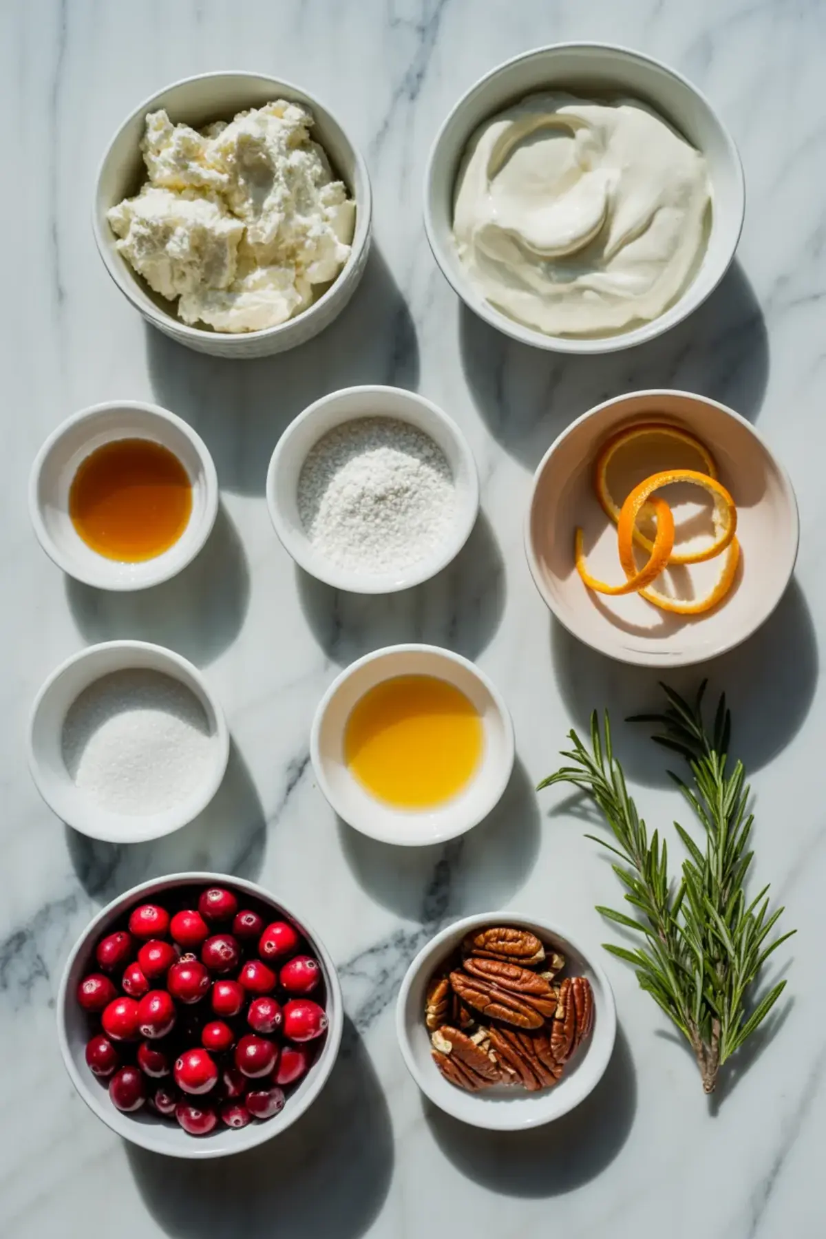 Ingredients for cranberry cream cheese dip arranged in bowls with fresh cranberries, cream cheese, sour cream, sugar, orange zest, rosemary, and chopped pecans.