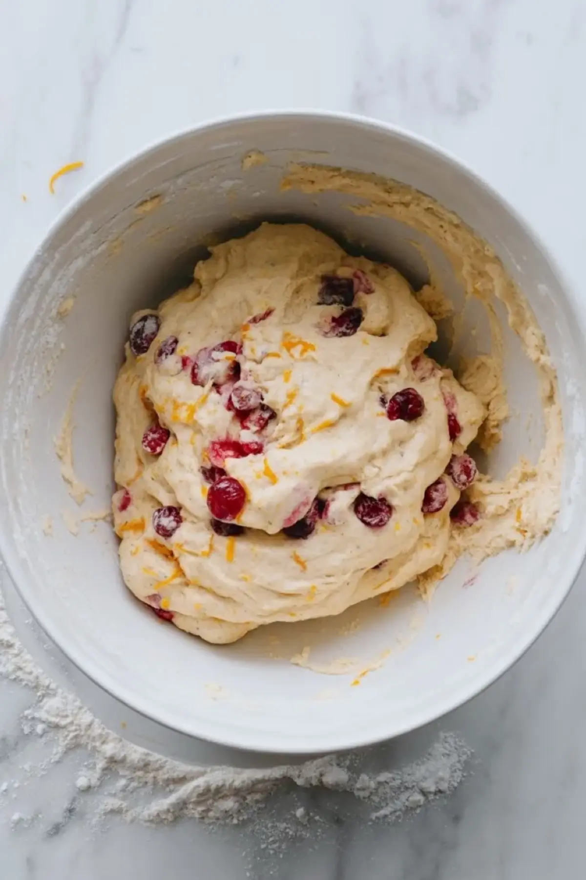 Cranberry orange scone dough mixed in a glass bowl with visible fresh cranberries and orange zest before shaping and cutting into wedges.