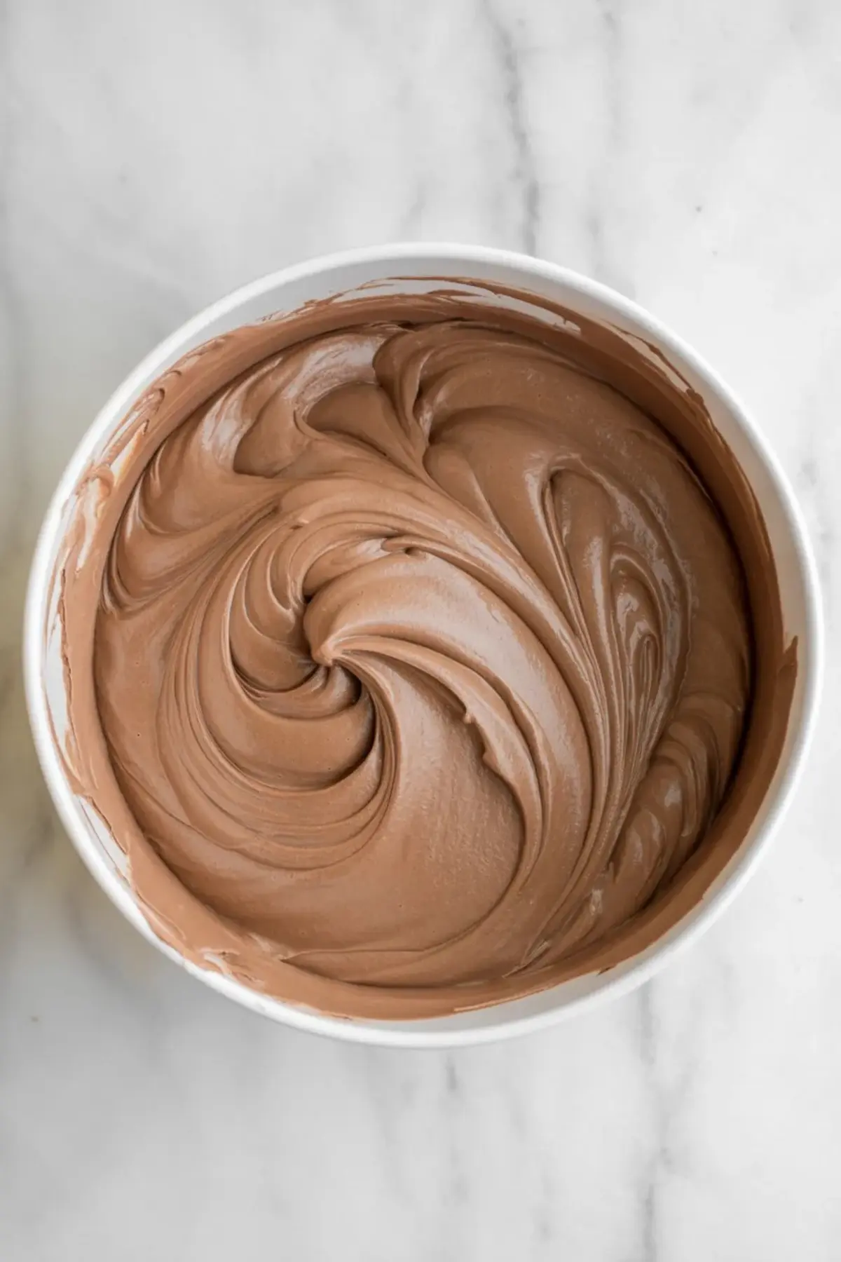 Smooth chocolate French silk filling swirled in a mixing bowl before spreading over the cooled brownie layer.