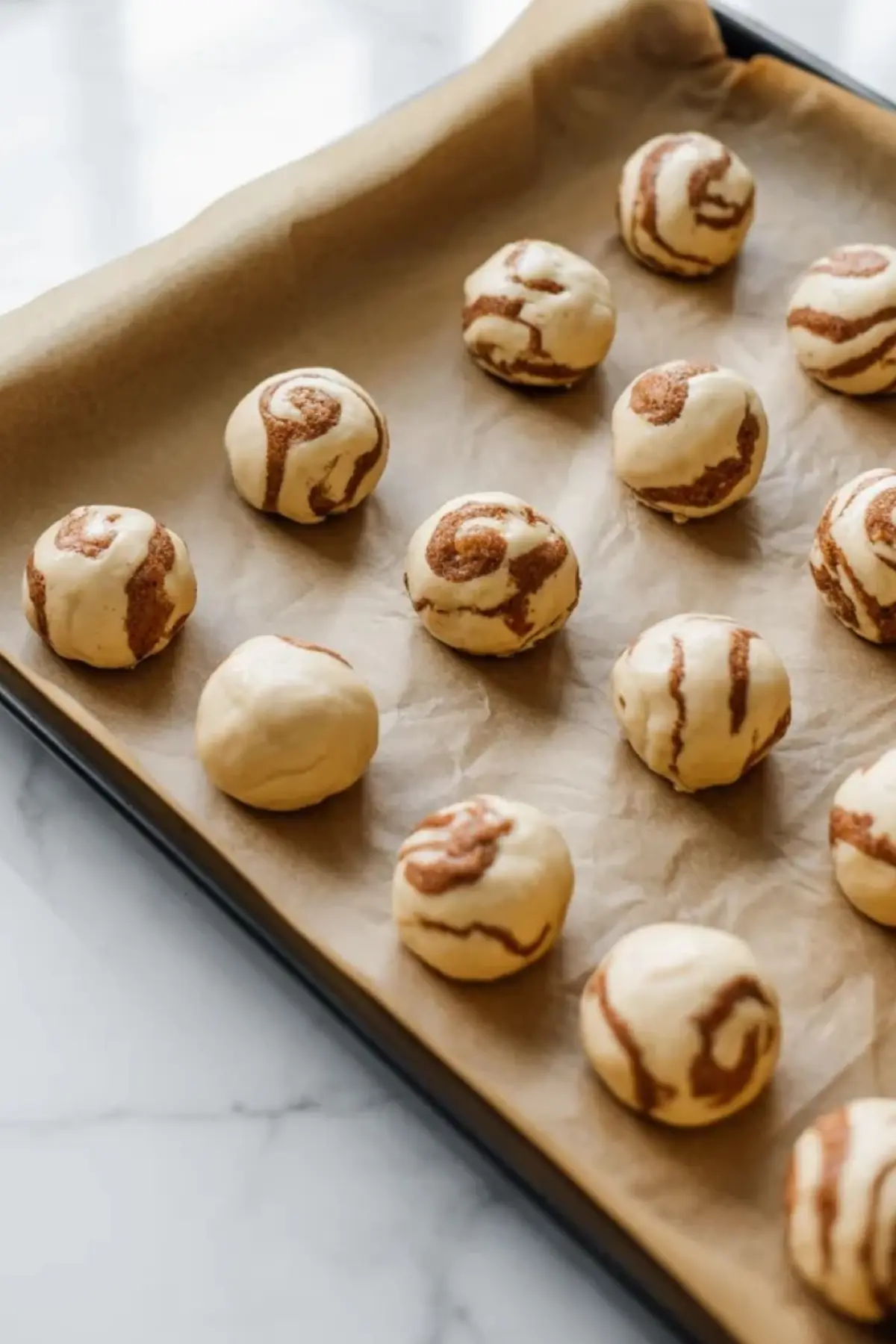 French toast cookie dough balls arranged on a parchment lined baking sheet before baking.
