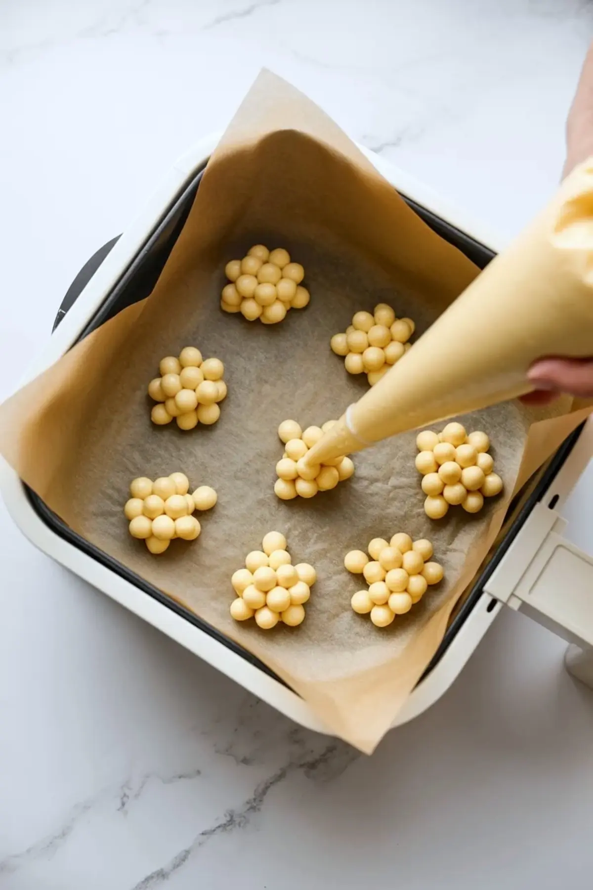 Air fryer funnel cake bite batter piped into small clusters on parchment inside the air fryer basket before cooking.