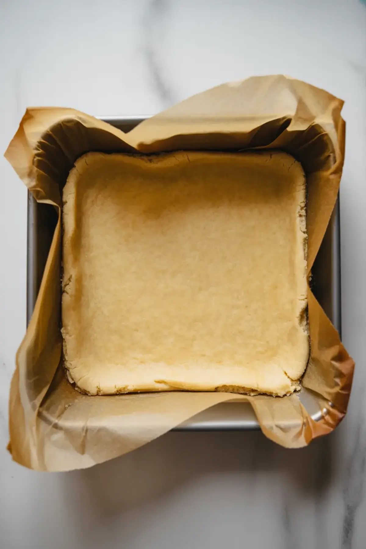 Baked shortbread crust in a parchment-lined square pan ready for hibiscus lemon filling.
